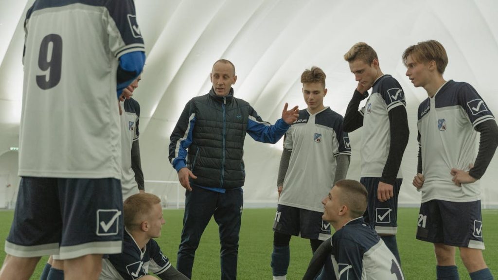 A coach passionately instructs his soccer team during a practice session inside a sports dome.