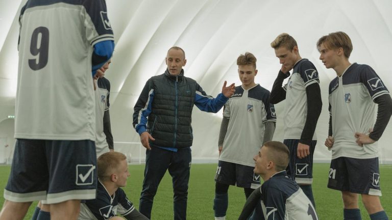 A coach passionately instructs his soccer team during a practice session inside a sports dome.